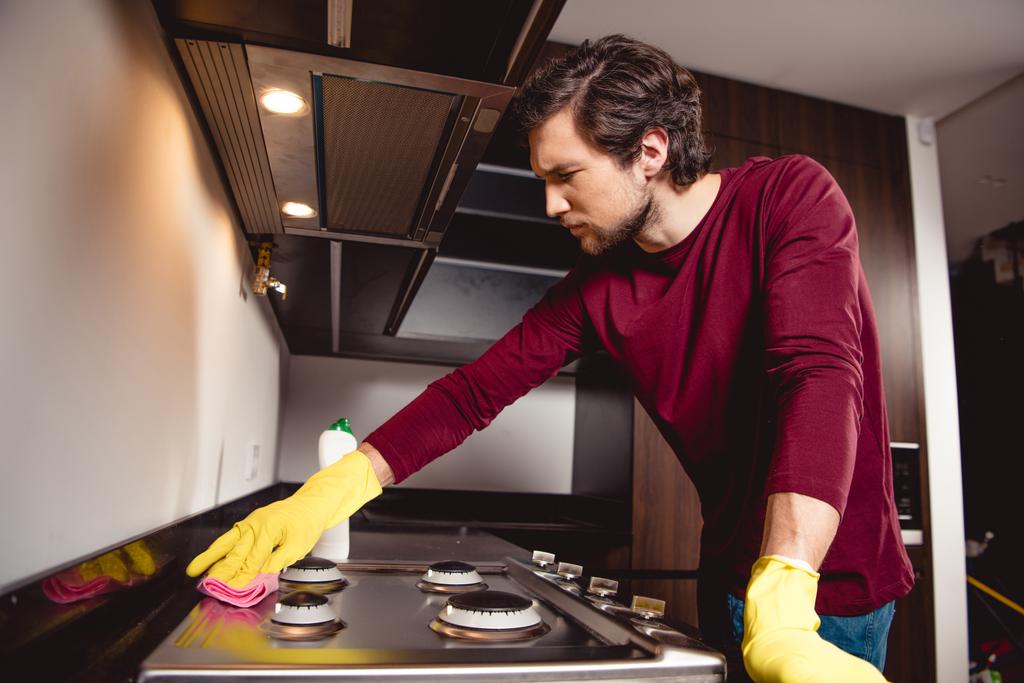 ernster Mann in Gummihandschuhen putzt Küche - Foto, Bild