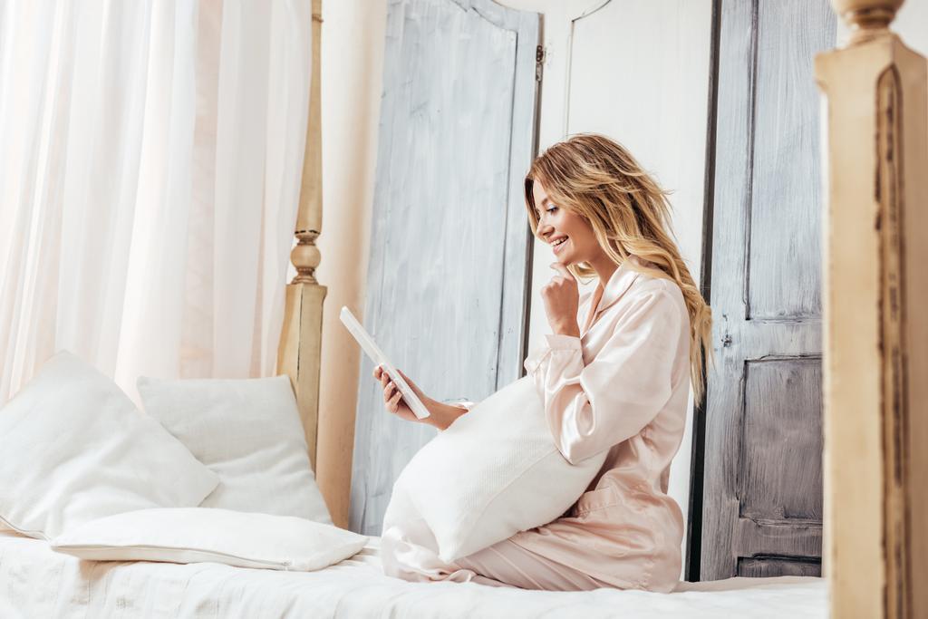 Genç kadın evde yatakta dijital tablet kullanarak yan görünüm - Fotoğraf, Görsel