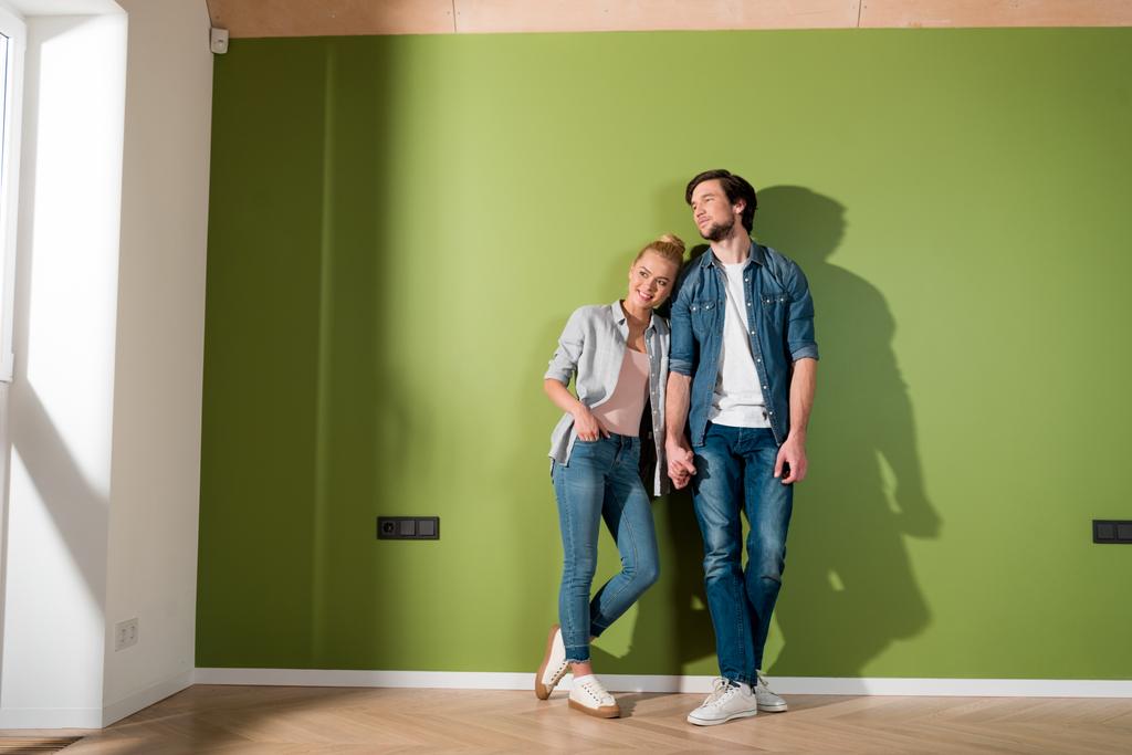aantrekkelijk meisje en knappe man hand in hand en permanent door groene muur - Foto, afbeelding