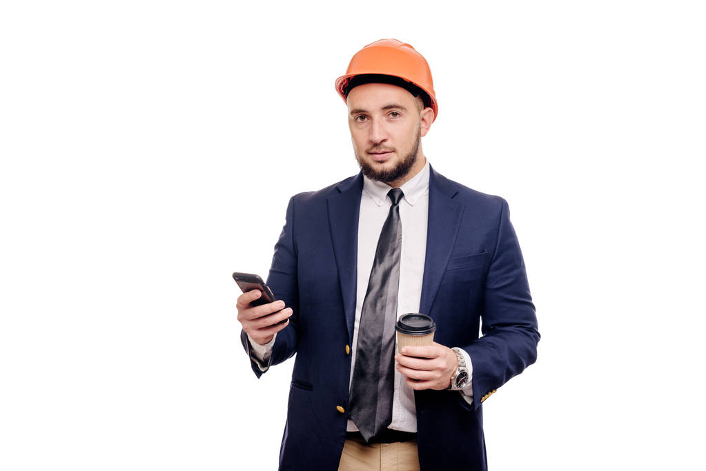 Retrato de negocios del contratista y desarrollador sorprendido, hablando de teléfono. Empresario en sombrero duro con taza de café de pie sobre fondo blanco. Concepto de freno de café y noticias
 - Foto, Imagen