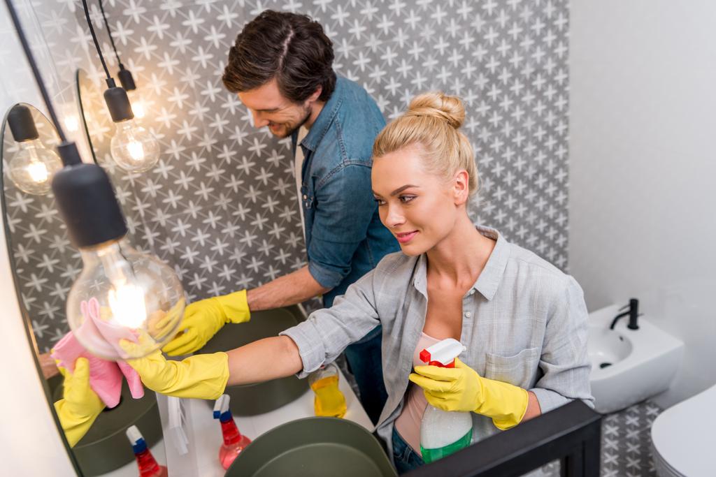 sonriente pareja en guantes de goma limpiando espejos en el baño
 - Foto, Imagen