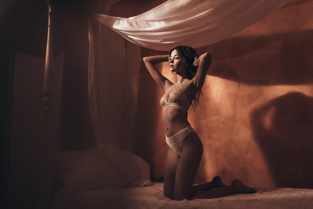 hübsche junge Frau trägt sexy beige Dessous und posiert im Bett - Foto, Bild