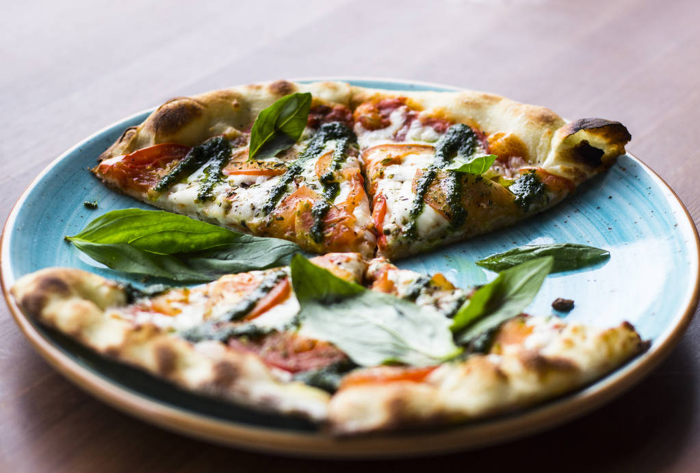 Viipaloitu Pizza Margarita tai Margherita sijaitsee sininen levy vastaan puinen pöytä tausta, ylhäältä katsottuna. Pizza tomaattien, tuoreen basilikan, mozzarellajuuston, pippurin ja mausteiden kanssa lähikuva. Perinteinen italialainen ruoka
. - Valokuva, kuva
