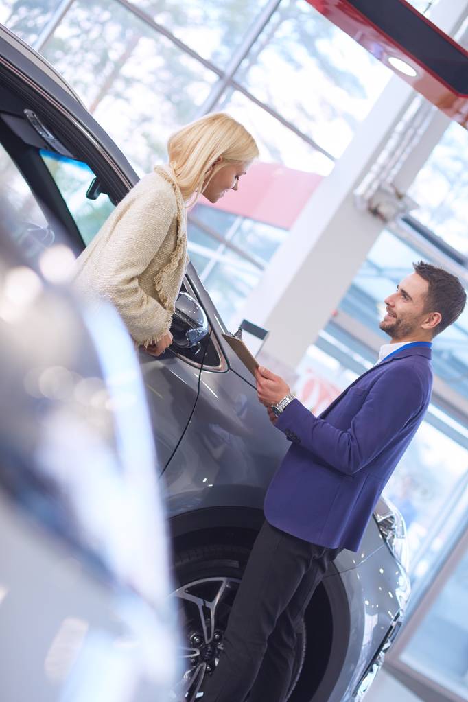 Handelaar met vrouw staat in de buurt van een nieuwe auto in de showroom - Foto, afbeelding