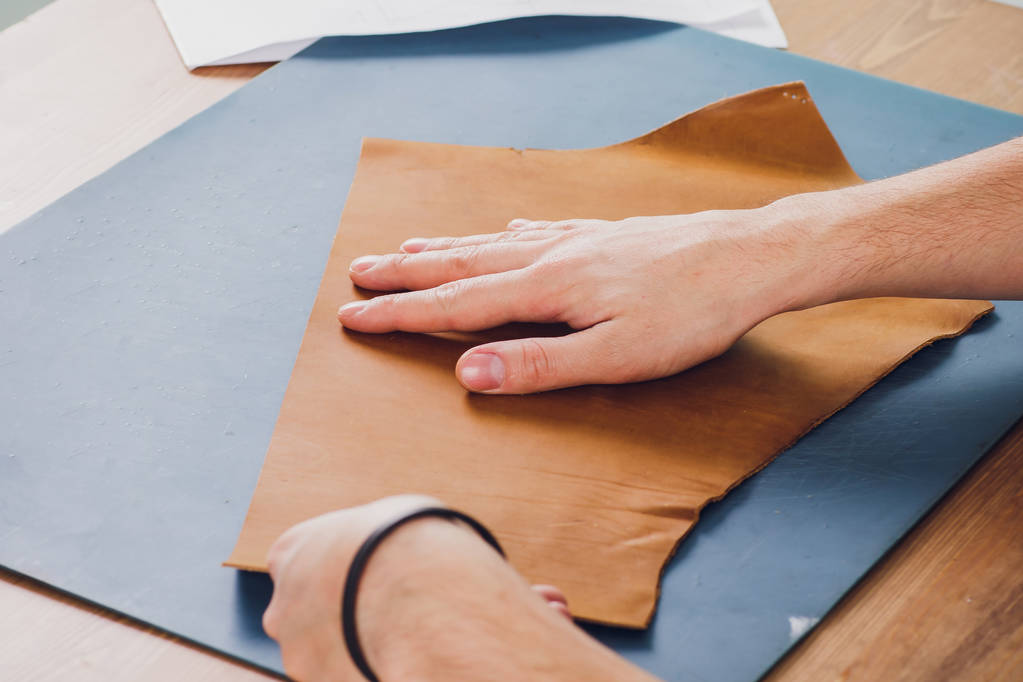 Journée de travail en studio. Homme travailleur du cuir dessin croquis de sac à main avec des portefeuilles en cuir et des outils pour la couture
. - Photo, image