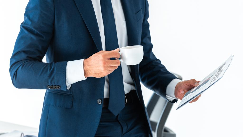 abgeschnittenes Bild eines Geschäftsmannes mit Tasse Kaffee und Zeitung isoliert auf Weiß - Foto, Bild