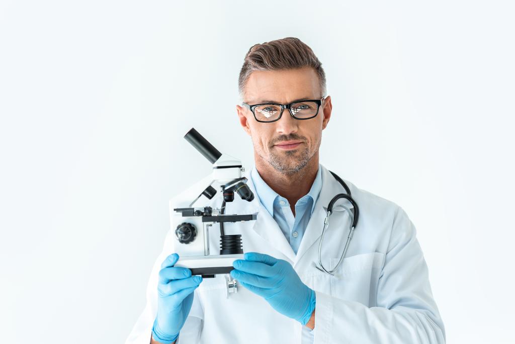 guapo científico en gafas sosteniendo microscopio y mirando a la cámara aislada en blanco
 - Foto, Imagen