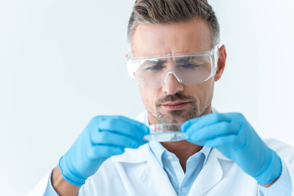 portrait of handsome scientist in protective glasses looking at reagent during experiment isolated on white - Photo, Image