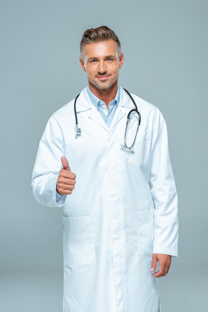 handsome doctor with stethoscope showing thumb up and looking at camera isolated on white - Photo, Image