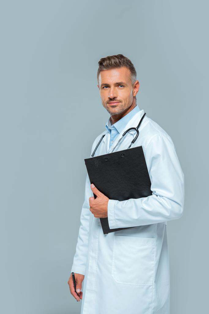 guapo médico con estetoscopio y portapapeles mirando a la cámara aislada en gris
 - Foto, Imagen