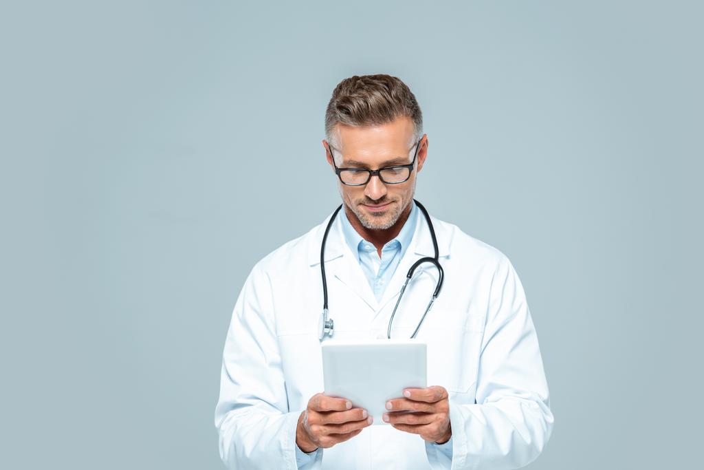 handsome doctor with stethoscope looking at tablet isolated on white - Photo, Image
