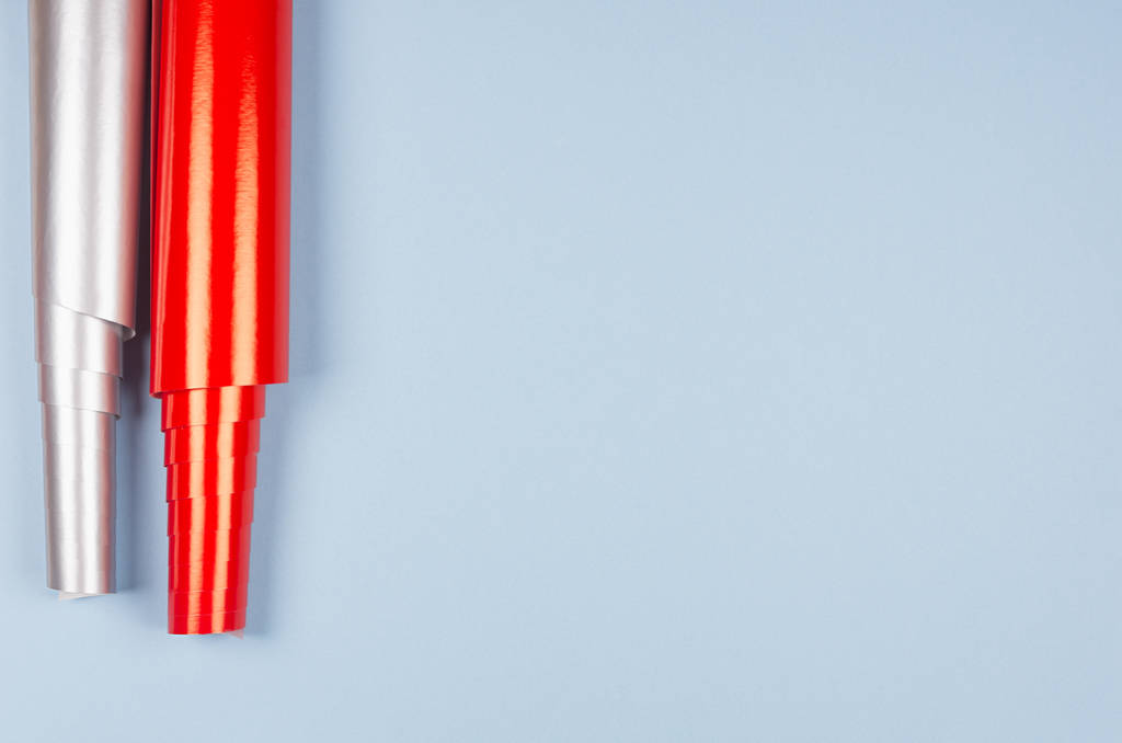 Rotoli di carta da imballaggio rosso e argento brillante su morbido sfondo blu pastello con spazio di copia, vista dall'alto
. - Foto, immagini