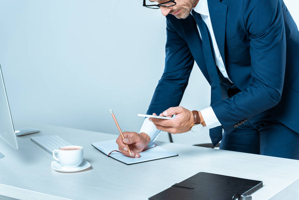 cropped image of businessman looking at smartphone and writing something isolated on white - Photo, Image