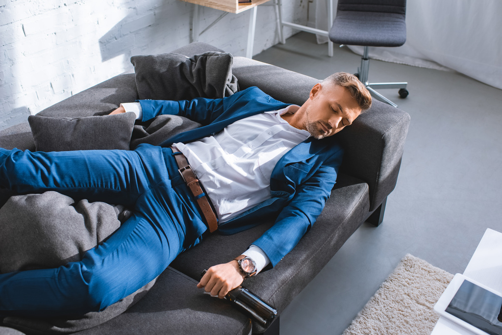 пьяный бизнесмен держит бутылку и отдыхает на диване в гостиной
  - Фото, изображение