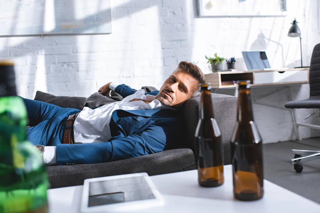 hombre de negocios borracho acostado en el sofá cerca de la mesa de café con botellas
 - Foto, Imagen