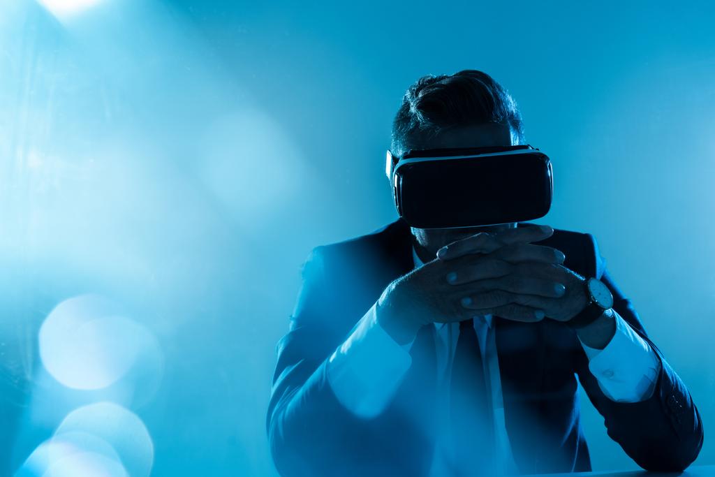 businessman in virtual reality headset sitting isolated on blue, artificial intelligence concept - Photo, Image