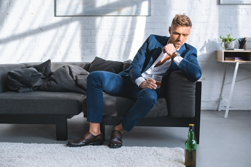 töprengő üzletember ül a kanapén, és a gazdaság üveg alkohol ital  - Fotó, kép