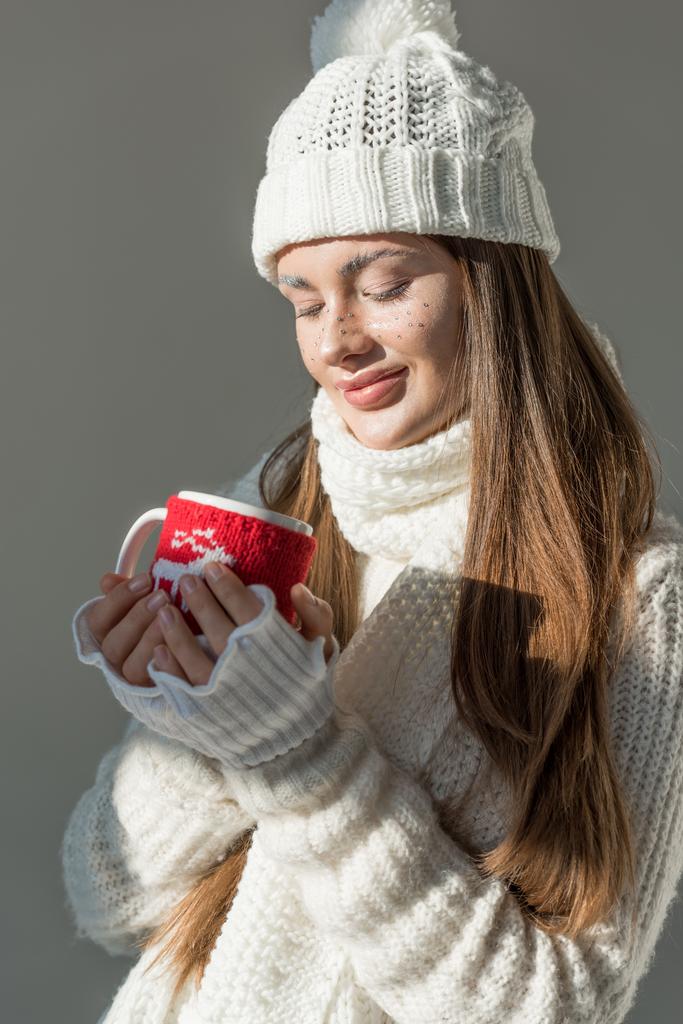 beautiful girl in stylish winter sweater and scarf holding cup of tea isolated on grey - Photo, Image