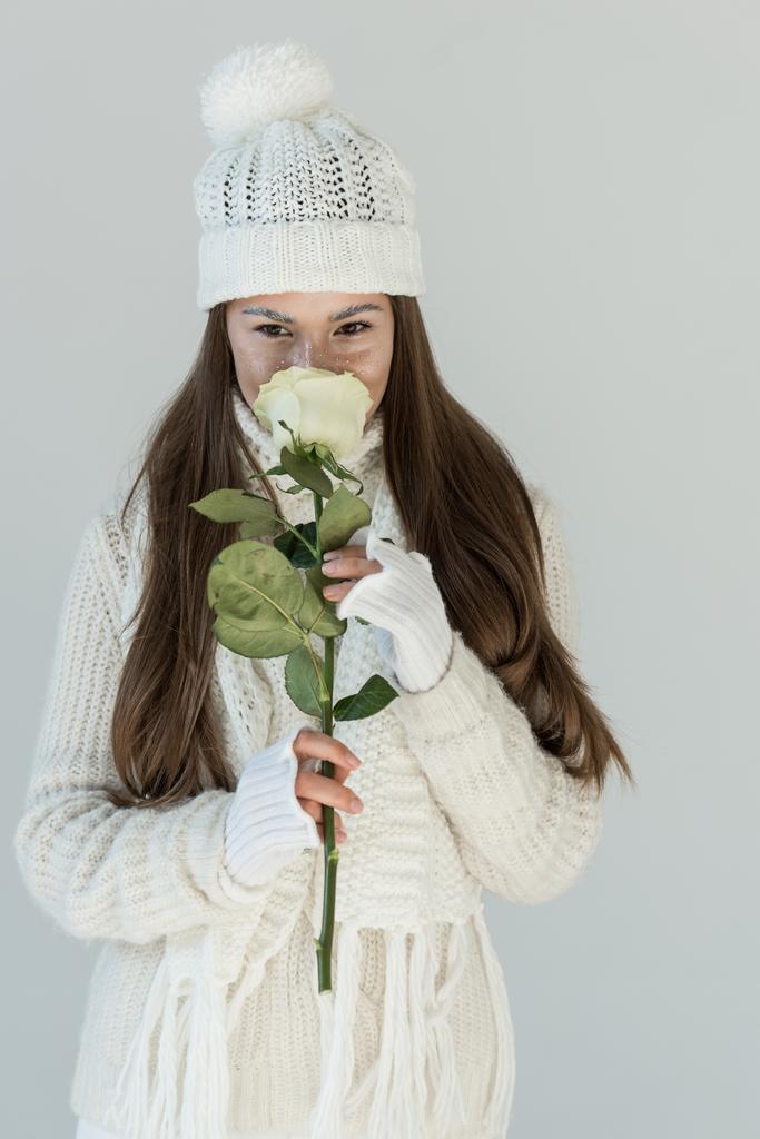 schöne Mädchen in modischen Winterpullover und Schal schnüffelnde weiße Rose und Blick in die Kamera isoliert auf weiß - Foto, Bild