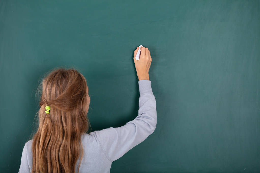 Rückansicht einer Studentin, die mit Kreide auf grüner Tafel schreibt - Foto, Bild