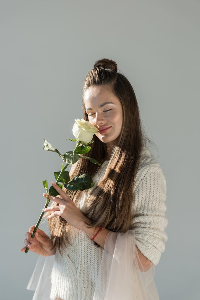 attraktive Frau im modischen Winteroutfit, die weiße Rose schnüffelt, mit geschlossenen Augen, isoliert auf weiß - Foto, Bild