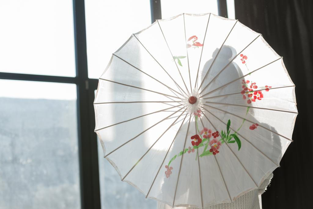 силуэт женщины, стоящей с бумажным зонтиком возле окна
 - Фото, изображение