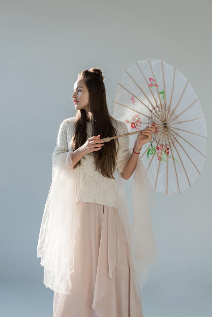 attractive woman in trendy winter outfit standing with japanese umbrella and looking away on white - Photo, Image