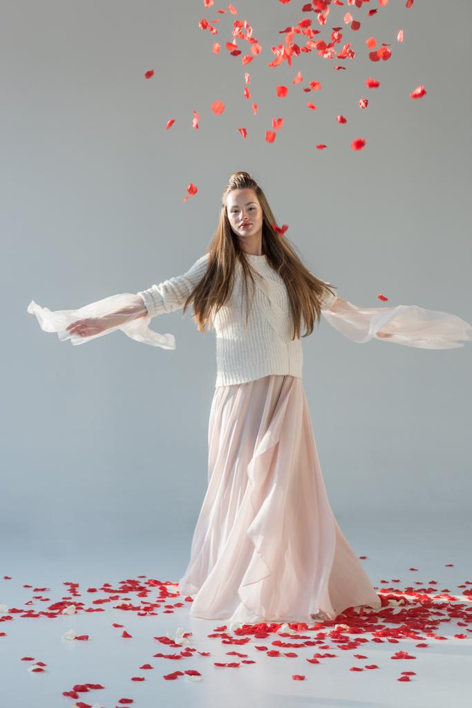 mulher atraente na roupa de inverno na moda girando em torno de pétalas de rosas vermelhas caindo isoladas em branco
 - Foto, Imagem