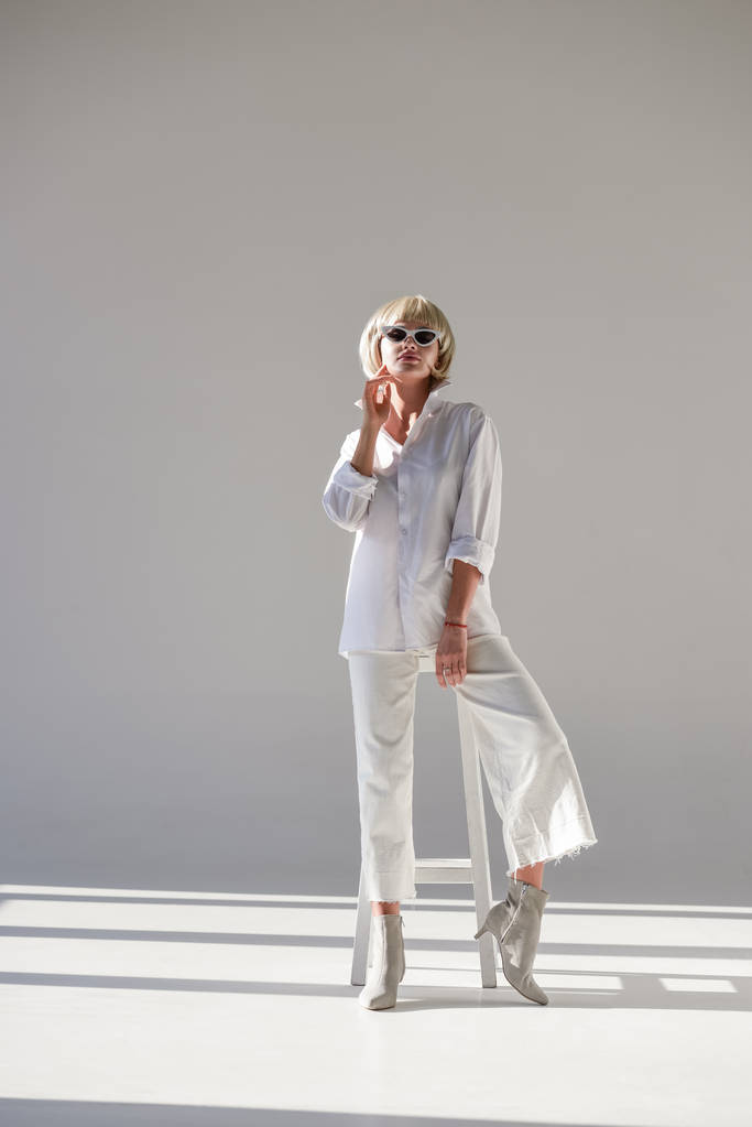 gyönyörű szőke lány napszemüveg és divatos fehér ruhában pózol a fehér - Fotó, kép