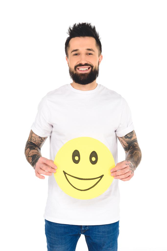 przystojny, brodaty mężczyzna z tatuażami, posiadający żółtą kartkę z wyrażenie szczęśliwy twarz patrząc na kamery na białym tle - Zdjęcie, obraz