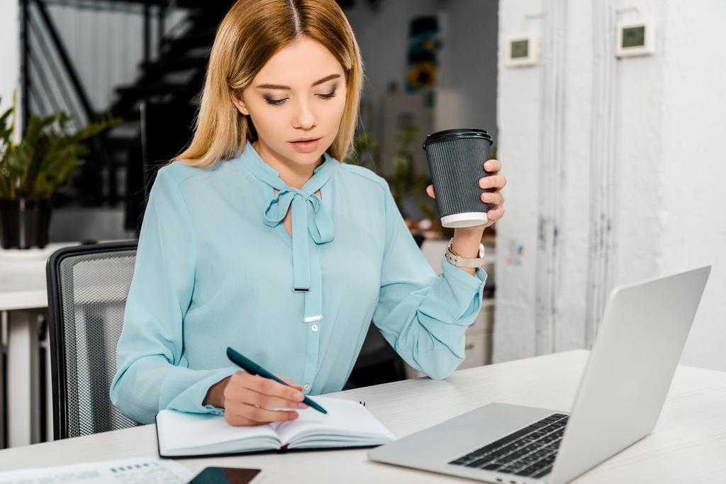 portrait of businesswoman with coffee to go at workplace with laptop and notebook - Photo, Image