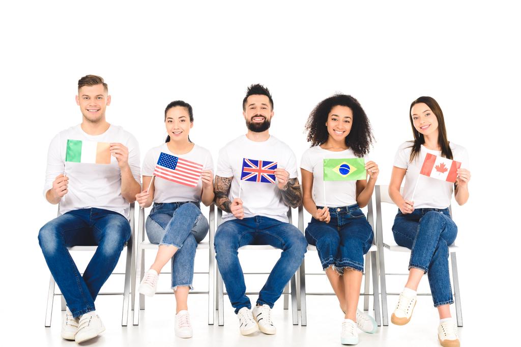 πολυπολιτισμική ομάδα των ανθρώπων που κάθονται στις καρέκλες με σημαίες των διαφορετικών χωρών που απομονώνονται σε λευκό - Φωτογραφία, εικόνα