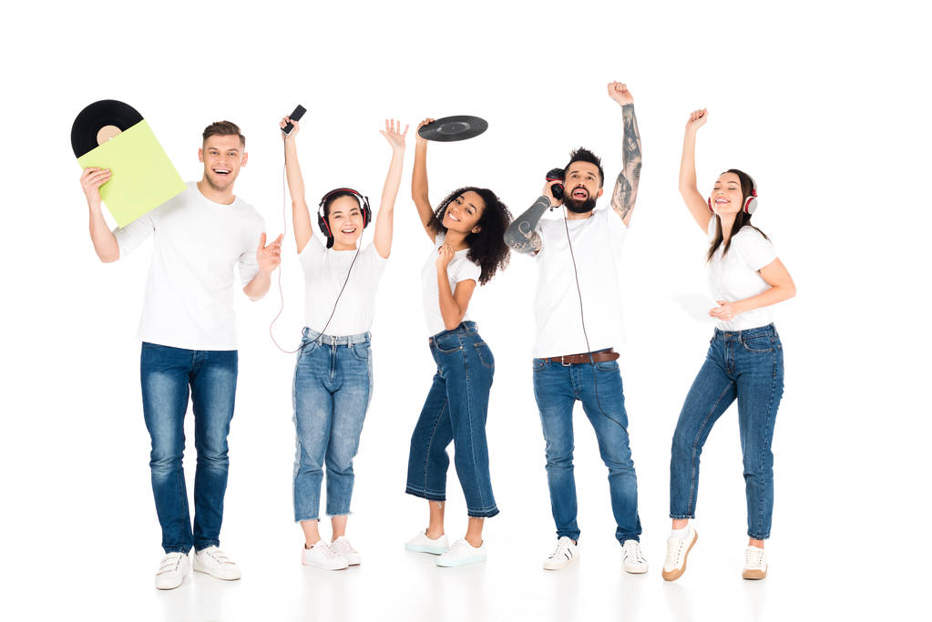 мультикультурная группа молодых людей с поднятыми руками слушает музыку в наушниках и держит виниловые пластинки изолированы на белом
 - Фото, изображение