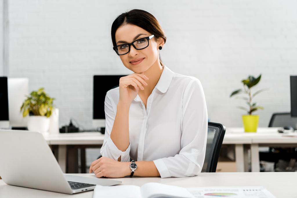Porträt einer lächelnden Geschäftsfrau mit Brille am Arbeitsplatz mit Laptop im Büro - Foto, Bild
