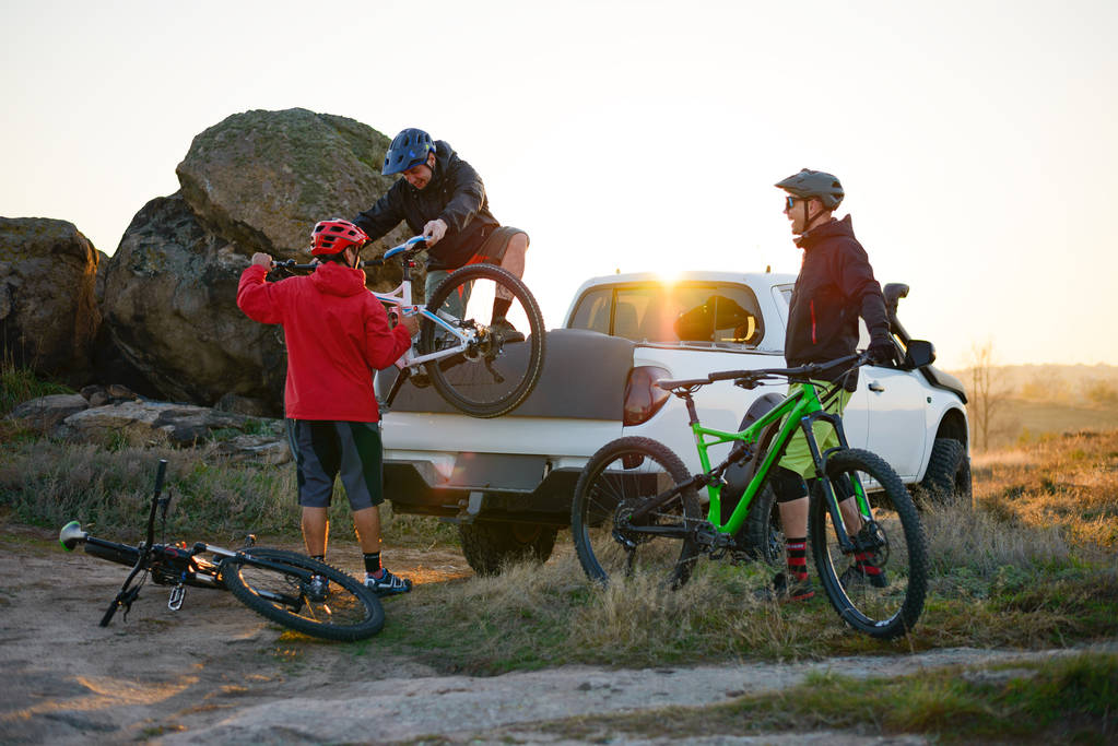 Freunde, die bei Sonnenuntergang MTB-Fahrräder vom Pickup-Geländewagen in die Berge bringen. Abenteuer und Reisekonzept. - Foto, Bild