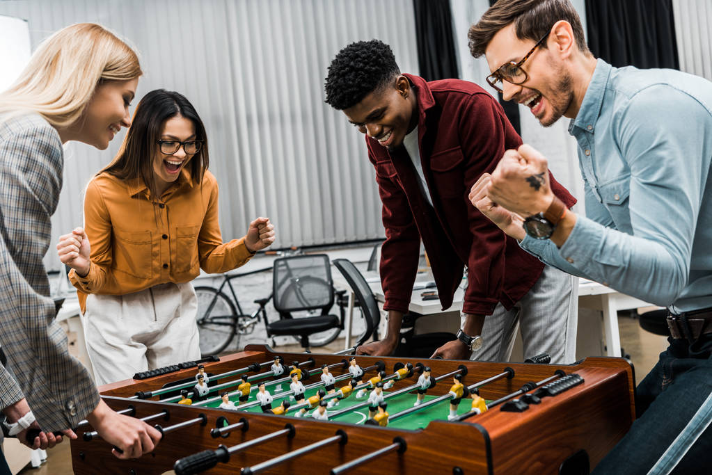 Коллеги по мультикультурному бизнесу вместе играют в настольный футбол в офисе
 - Фото, изображение