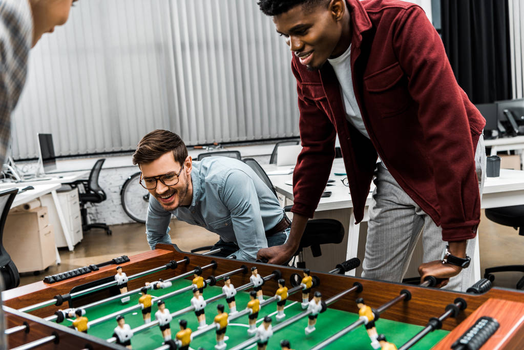smiling multicultural businessmen playing table football in office - Photo, Image