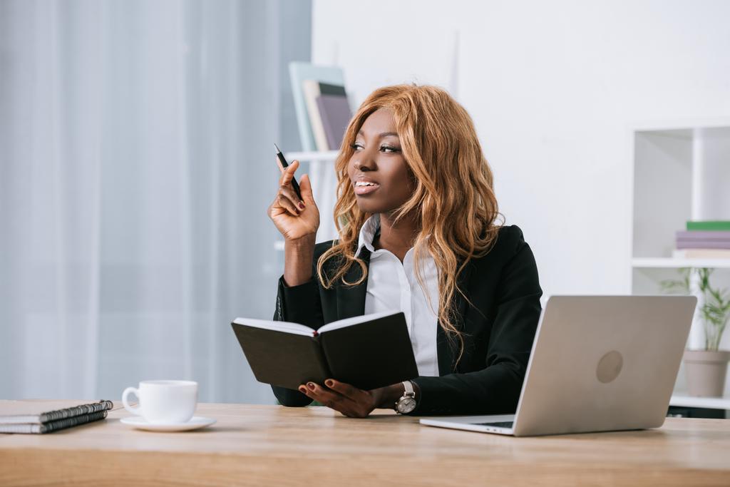 beautiful african american businesswoman holding notebook and pen in modern office  - Photo, Image