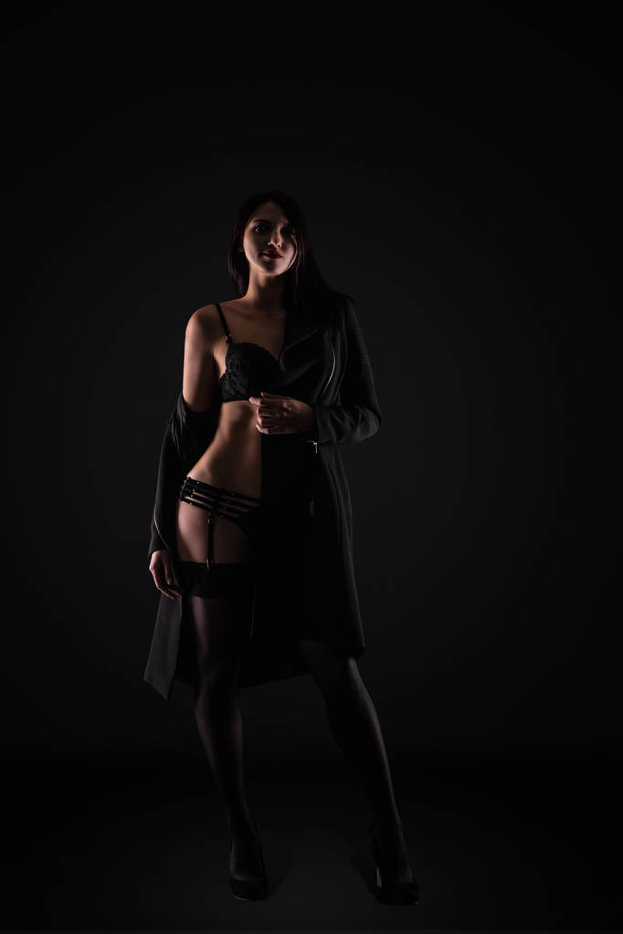 ポーズ スタジオで黒の背景の壁に黒の官能的なランジェリーでセクシーな若いブルネットの女性. - 写真・画像