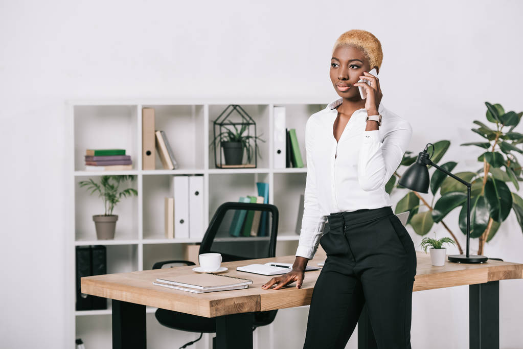 Африканская американская бизнесвумен с короткими волосами разговаривает на смартфоне в современном офисе
 - Фото, изображение