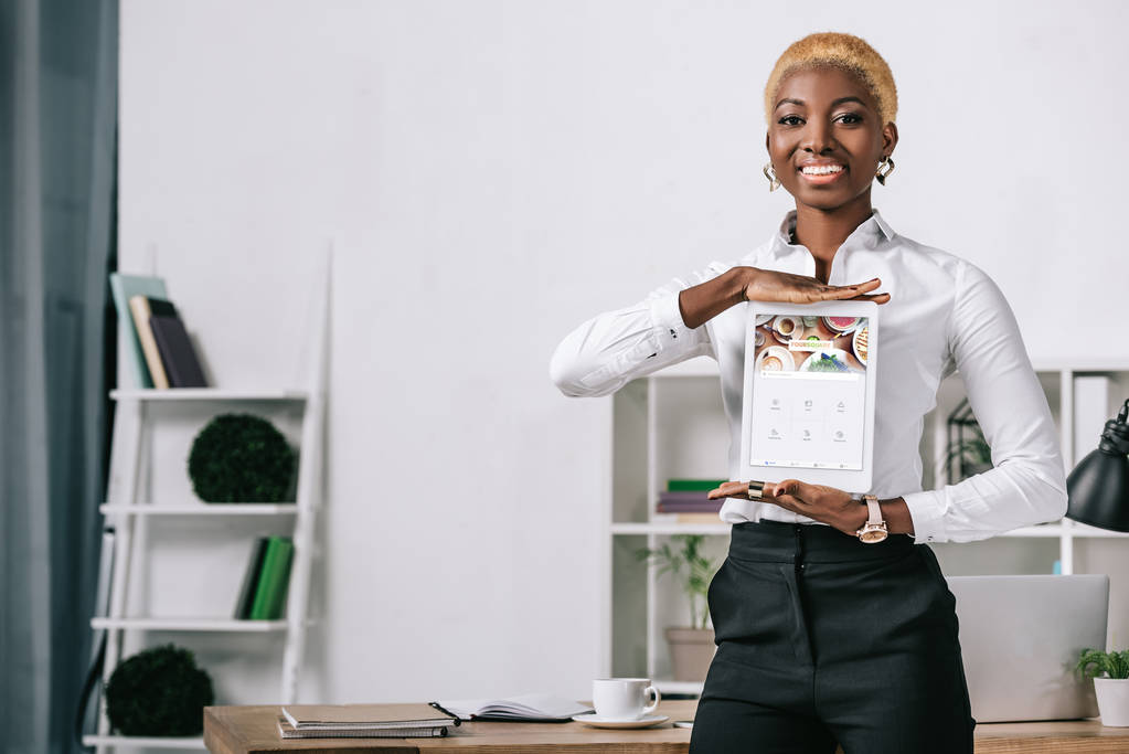 alegre mujer afroamericana mostrando tableta digital con aplicación cuadrada en la pantalla
  - Foto, Imagen