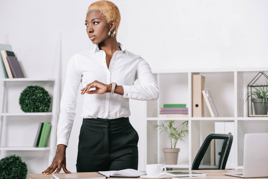серьезная африканская американская бизнесвумен с короткими волосами, стоящая у стола в современном офисе
 - Фото, изображение