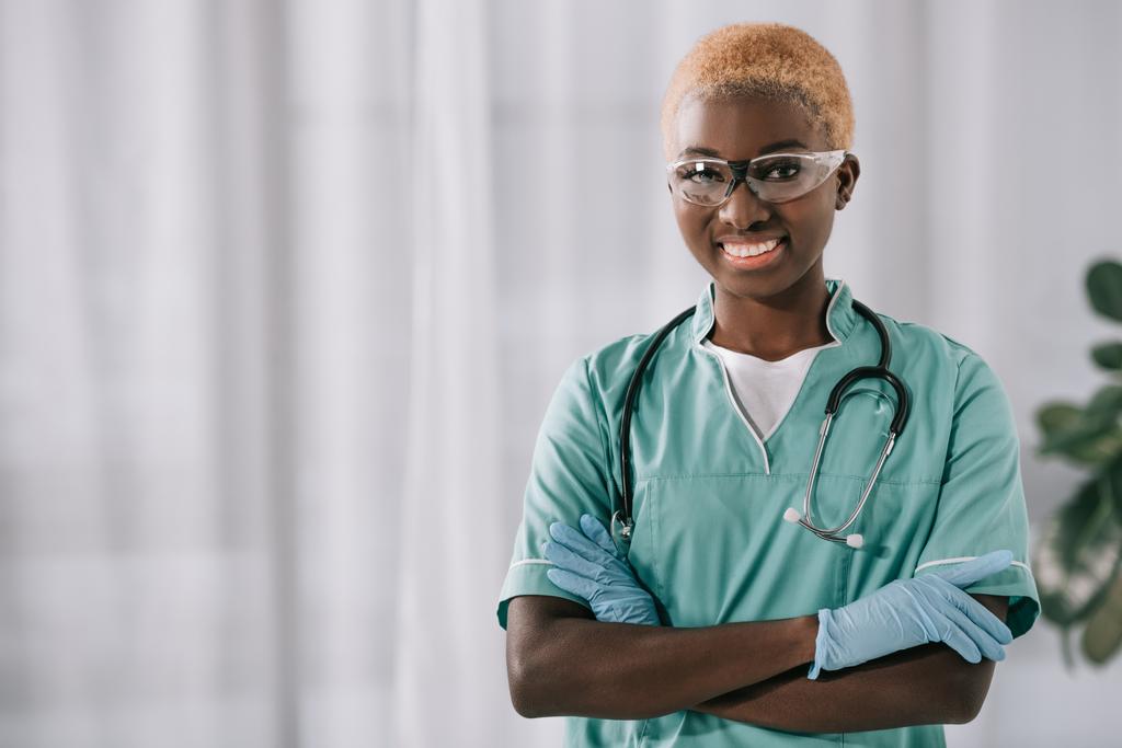 mosolygó afro-amerikai nővér, a kesztyű állandó keresztezett karokkal, miközben nézi a kamera - Fotó, kép