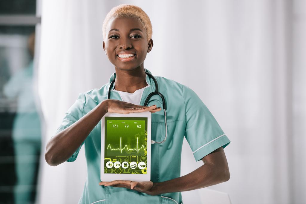 enfermera afroamericana sonriente con estetoscopio sosteniendo tableta digital con ritmo cardíaco en pantalla
 - Foto, imagen