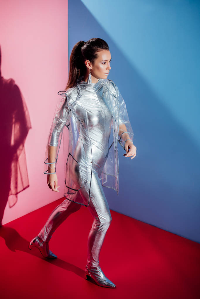 beautiful elegant model posing in silver bodysuit and raincoat on pink and blue background - Photo, Image