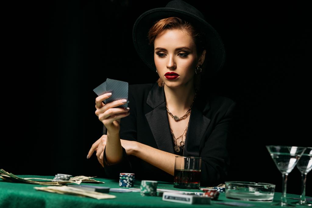 attraktives Mädchen in Jacke und Hut, das Poker spielt und im Casino Karten betrachtet - Foto, Bild