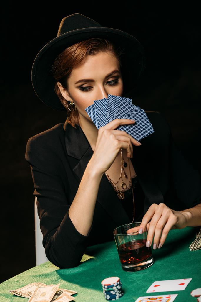 attraktives Mädchen in Jacke und Hut, das Gesicht mit Pokerkarten im Casino verdeckt - Foto, Bild
