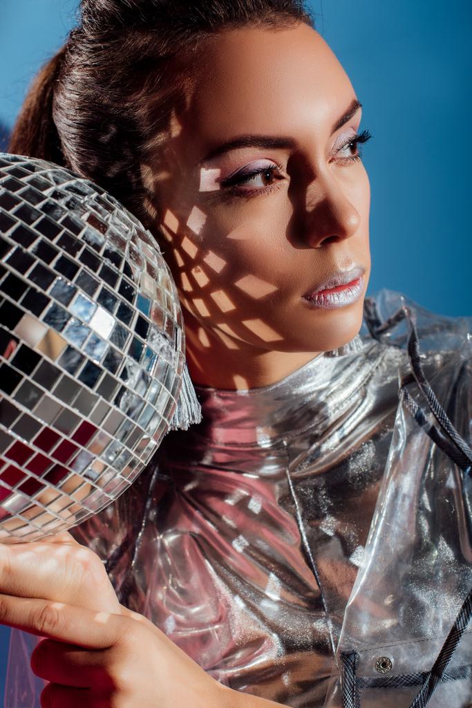 aantrekkelijke jonge vrouw poseren met zilver disco bal op blauwe achtergrond - Foto, afbeelding