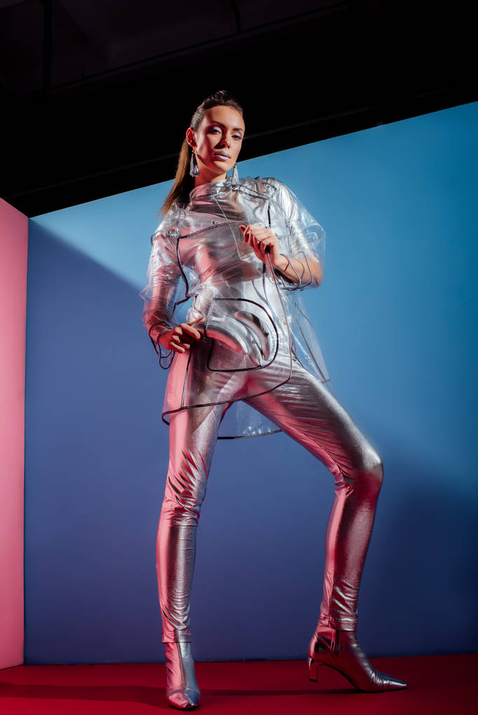 divatos fiatal nő a fémes Body és esőkabátot, pózol kék alapon ezüst banánnal - Fotó, kép
