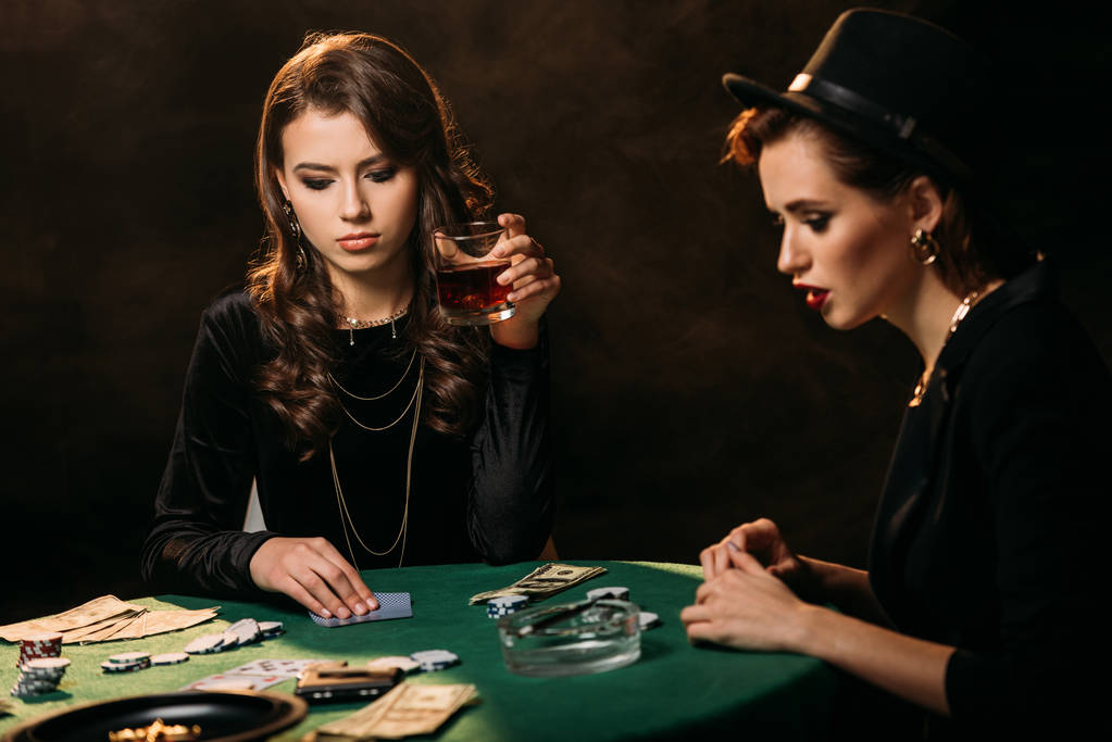 chicas atractivas jugando al póquer en la mesa en el casino, mujer sosteniendo un vaso de whisky
 - Foto, Imagen